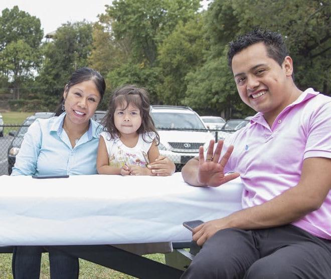 A father, mother, and a toddler sitting at a table outside.